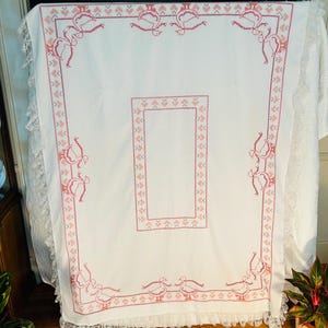 Puede incluir: Mantel blanco con un dise&ntilde;o bordado en rosa con p&aacute;jaros y patrones geom&eacute;tricos. El mantel tiene un ribete de encaje en los bordes. El dise&ntilde;o es sim&eacute;trico y cubre el borde y un &aacute;rea rectangular central.