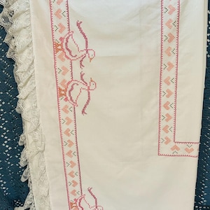 Puede incluir: Mantel de lino blanco con bordado de punto de cruz rosa. El bordado presenta un borde de corazones y gansos, con un ribete de encaje en el borde. El dise&ntilde;o es de estilo cl&aacute;sico y vintage.