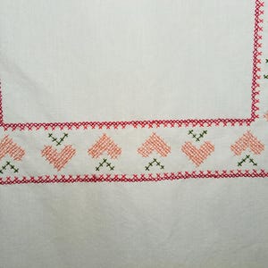 Puede incluir: Tela blanca con un borde de punto de cruz rojo y verde. El borde presenta corazones de color melocot&oacute;n y detalles verdes de punto de cruz. Las esquinas tienen un dise&ntilde;o similar, creando un patr&oacute;n cohesivo.