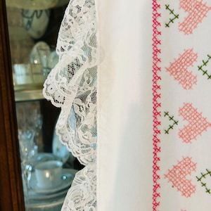 Puede incluir: Tela blanca con un delicado ribete de encaje en el lado izquierdo. El lado derecho presenta un dise&ntilde;o de punto de cruz de corazones rosas y detalles verdes, creando una est&eacute;tica vintage.