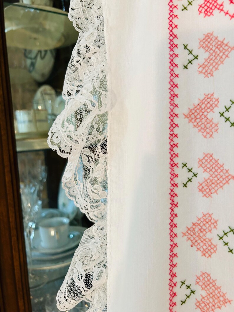 Puede incluir: Tela blanca con un delicado ribete de encaje en el lado izquierdo. El lado derecho presenta un dise&ntilde;o de punto de cruz de corazones rosas y detalles verdes, creando una est&eacute;tica vintage.