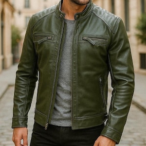 Op de afbeelding: Olijfgroene leren jas met een opstaande kraag, ritssluiting en meerdere ritszakken. De jas heeft een gewatteerd schouderontwerp en een getailleerde pasvorm. Het model draagt er een grijs t-shirt onder.