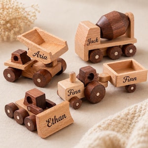 Puede incluir: Un conjunto de cuatro vehículos de juguete de madera: un camión volquete, una hormigonera, un tractor con remolque y una excavadora. Cada juguete está hecho de madera clara y oscura y tiene los nombres "Aria", "Jack", "Finn" y "Ethan".