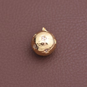May include: A gold-colored soccer ball pendant with a small loop for a chain. The pendant is adorned with small, sparkling gemstones. The soccer ball design is detailed with hexagonal and pentagonal shapes.