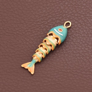 May include: A fish-shaped pendant featuring a turquoise and orange enamel finish with a textured gold-tone metal skeleton design. The charm includes a small circular loop at the top for attachment and a single orange accent dot for the eye.
