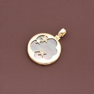 Op de afbeelding: Een goudkleurige hanger met een rond ontwerp met een wolkvorm en drie steruitsparingen. Twee sterren zijn versierd met kleine, heldere edelstenen. De hanger heeft een parelmoer, iriserend midden en een lus voor een ketting.