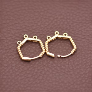 May include: Two gold-colored, hexagonal earring components. Each component has a small loop at the top and a curved, open bottom. One side of each hexagon is decorated with a twisted rope design.