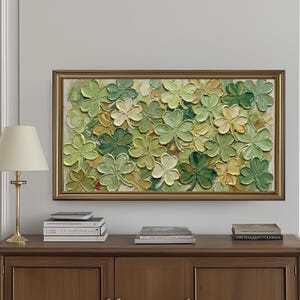 May include: A framed artwork featuring a textured, three-dimensional depiction of green and yellow shamrocks. The artwork is displayed above a wooden cabinet with three doors. A gold lamp and books are on the cabinet.