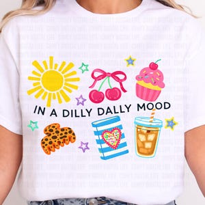 May include: White t-shirt with colorful graphic illustrations including a yellow sun, cherries, cupcake, cookie, book, and iced coffee. The text "IN A DILLY DALLY MOOD" is printed below the illustrations.