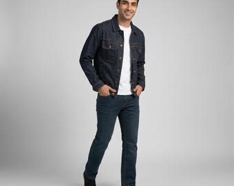 May include: A dark blue denim jacket with a collar and button-front closure, worn over a plain white t-shirt. The outfit includes dark blue denim jeans and black sneakers. The jacket features two chest pockets with buttoned flaps and long sleeves.