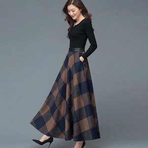 May include: A long-sleeved black top paired with a high-waisted, floor-length maxi skirt featuring a large brown and navy blue plaid pattern. The skirt has a fitted waistband and side pockets, creating a full, flared silhouette.