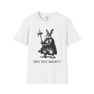 May include: White t-shirt featuring a black and white illustration of a rabbit in armor holding a battle axe. The text "TINY BUT MIGHTY" is printed below the illustration. The shirt has a crew neck and short sleeves.