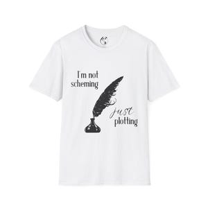 May include: White t-shirt with a black graphic of a quill pen and inkwell. The text on the shirt reads "I'm not scheming just plotting". The shirt has a crew neck and short sleeves.