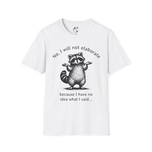 May include: White t-shirt featuring a black and white illustration of a raccoon with its arms raised. The text on the shirt reads "No, I will not elaborate because I have no idea what I said..."