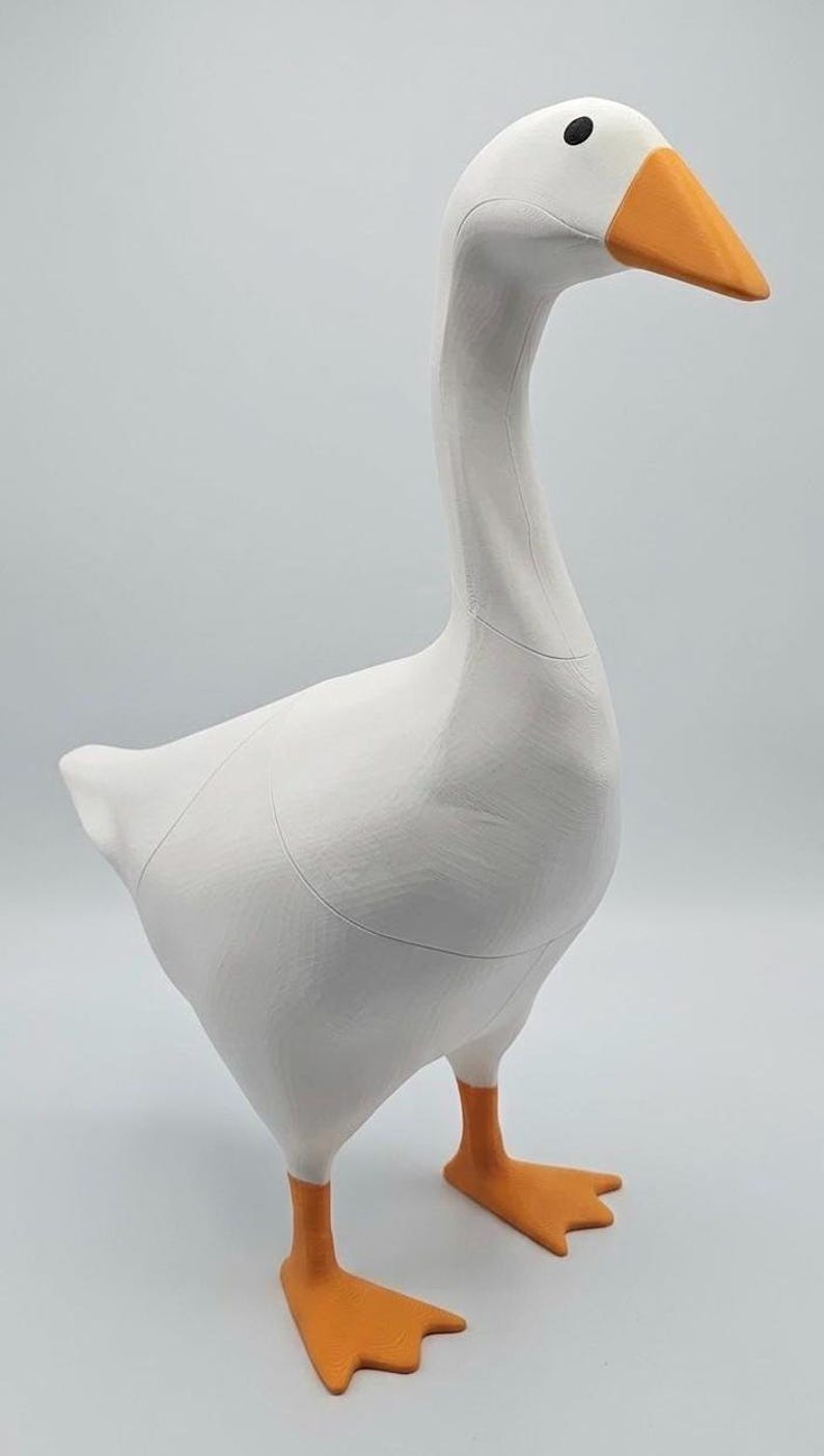 May include: A white goose figurine with an orange beak and feet. The goose has a long neck and is standing upright. The figurine is made of a smooth material and has a simple, clean design. The goose is a decorative item.
