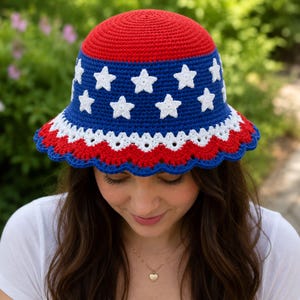 May include: A crochet bucket hat featuring a solid red crown, a blue band decorated with white star appliques, and a scalloped brim with alternating white and red layers finished with a blue edge, crafted in a dense, textured yarn stitch pattern.