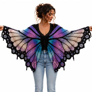 May include: A colorful, crochet butterfly wing wrap in shades of purple, blue, and cream. The wrap features a black neckline and edging with a scalloped design. The wings are spread wide, showcasing the intricate crochet work.