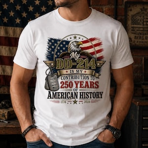 May include: A white t-shirt featuring a graphic of a bald eagle over an American flag. The text reads: My DD-214 IS MY CONTRIBUTION TO 250 YEARS OF AMERICAN HISTORY 1776-2026. Two silver military dog tags hang from the design with the text HONOR COURAGE COMMITMENT.