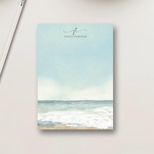 May include: A blue and white watercolor notepad with the text "jt Jessica Thornton" at the top. The notepad features a watercolor painting of a beach scene with waves crashing on the shore.