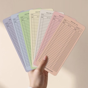 May include: A hand holds a fan of pastel-colored reading log cards. Each card has a different color, including lavender, blue, green, yellow, and peach. The cards are labeled with "Reading Log" and have spaces for book title, date, and rating.
