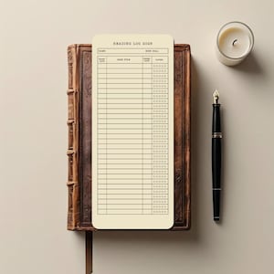 May include: A reading log for 2025 rests on a vintage book. The cream-colored log features columns for book title, start and finish dates, and a rating system. A lit candle and a black fountain pen complete the scene.