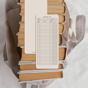May include: A stack of vintage books with aged, yellowed pages and a beige reading log. The reading log has a lined layout with the text "Reading Log" at the top. A beige tote bag is in the background.