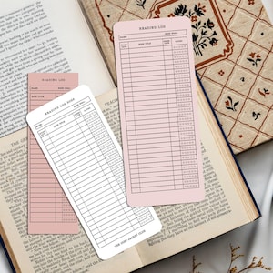 May include: A stack of pink reading log cards with lined spaces for recording book titles and ratings, placed among open books with decorative covers. The cards are designed for tracking reading progress.