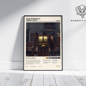 May include: A framed poster for "The French Dispatch" film. The poster features a scene from the movie with two figures in front of a building. The poster has a cream-colored background with black text and a color palette at the bottom.