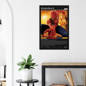 May include: A framed poster for the movie "Spider-Man 2" featuring the superhero in a dynamic pose. The poster has a black background with the movie title and year at the top. The image includes the director, writers, and cast.