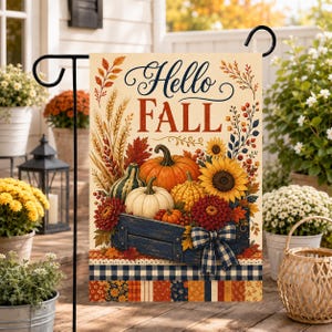 Puede incluir: Una bandera de jardín rectangular con el texto Hello Fall en letra azul oscuro y roja. El diseño muestra una caja de madera azul oscuro llena de calabazas, girasoles y follaje otoñal, acentuada por un lazo a cuadros azul y blanco.