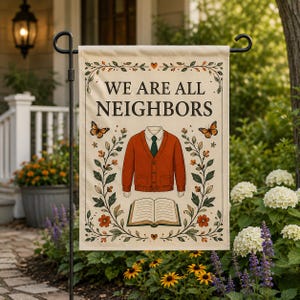 May include: A rectangular garden flag with a cream background featuring the text WE ARE ALL NEIGHBORS in black. The design includes a central orange cardigan, an open book, two monarch butterflies, and a decorative border of green vines and flowers.