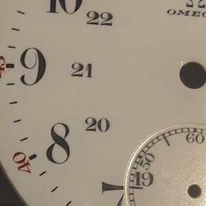 May include: Close-up of a vintage watch face with black numerals on a cream-colored background. The watch face includes a smaller subdial and the word "SWISS". The numbers 7, 8, 9, 10, 11, and 12 are visible.