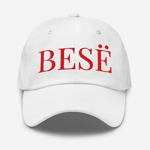 Könnte beinhalten: Weißes Baseball-Cap mit dem roten Wort "BESË" auf der Vorderseite gestickt. Die Kappe hat einen gebogenen Schirm und einen verstellbaren Riemen auf der Rückseite. Der Hut ist aus einem weichen, strapazierfähigen Stoff gefertigt.