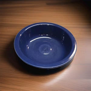 May include: A deep, circular bowl with a smooth, glossy finish in a solid dark blue color. The interior base of the bowl features a series of concentric circular embossed rings centered in the middle, providing a subtle textured detail.