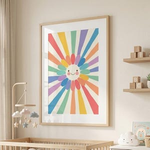 Pode incluir: Uma impressão artística emoldurada com um design de raio de sol sorridente em cores do arco-íris. A obra de arte está emoldurada em uma moldura de madeira clara. A imagem é exibida em um ambiente de berçário, com um berço e elementos decorativos.