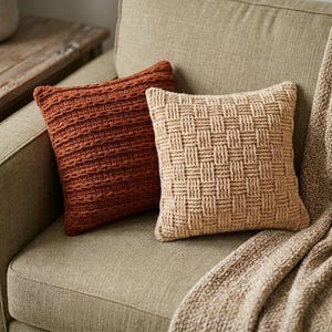 Puede incluir: Dos cojines cuadrados. Uno es de color naranja quemado intenso con una textura de punto acanalado horizontal. El segundo es de color beige claro y presenta un patrón de tejido de cesta prominente en toda la superficie frontal.