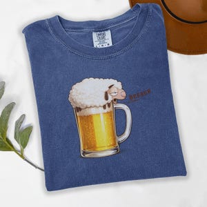 May include: Blue t-shirt with a cartoon illustration of a sheep's head atop a beer mug filled with golden beer. The word "BEEEEEER" is printed in red. The shirt has a Comfort Colors tag.