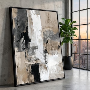 Puede incluir: Impresión artística abstracta en un marco negro. La obra presenta un diseño texturizado con pinceladas verticales en tonos de negro, blanco, gris y beige. El arte enmarcado está apoyado contra una pared de hormigón.