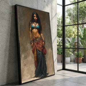 Puede incluir: Una obra de arte enmarcada que representa a una mujer con un sujetador turquesa y una falda a capas en tonos rojos, amarillos y azules. La mujer tiene el pelo largo y negro y está adornada con joyas. La obra de arte está apoyada contra una pared de hormigón cerca de una ventana con plantas.