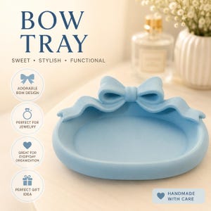 May include: A light blue circular tray featuring a decorative bow design on the rim. The text on the image reads: BOW TRAY, SWEET • STYLISH • FUNCTIONAL, ADORABLE BOW DESIGN, PERFECT FOR JEWELRY, GREAT FOR EVERYDAY ORGANIZATION, PERFECT GIFT IDEA, HANDMADE WITH CARE.