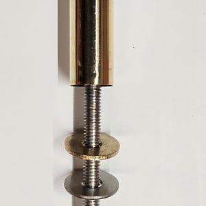 May include: A brass-colored cylindrical object with a threaded metal rod, two washers, and a nut. The cylindrical piece has a rounded top. The washers are gold and silver. The nut is silver.