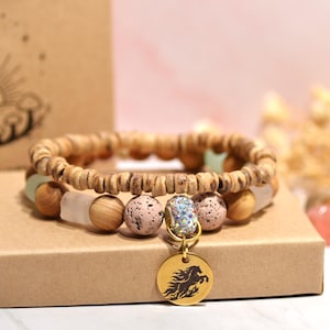 Op de afbeelding: Een houten kralenarmband met een gouden bedel met een paardensilhouet. De armband bevat lichtbruine, roze en heldere kralen. Een kleine fles met een zwarte dop en diverse kristallen staan ook op de foto.