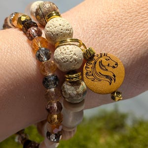 Pode incluir: Tr&ecirc;s pulseiras de contas em tons de castanho, dourado e transparente. Uma pulseira apresenta um berloque de madeira com um desenho de cabe&ccedil;a de cavalo. As contas incluem cristais facetados, rocha vulc&acirc;nica e contas de pedra estampadas. Detalhes met&aacute;licos dourados s&atilde;o usados.
