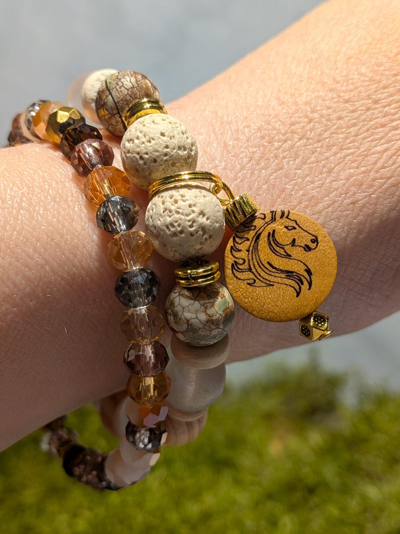 Pode incluir: Tr&ecirc;s pulseiras de contas em tons de castanho, dourado e transparente. Uma pulseira apresenta um berloque de madeira com um desenho de cabe&ccedil;a de cavalo. As contas incluem cristais facetados, rocha vulc&acirc;nica e contas de pedra estampadas. Detalhes met&aacute;licos dourados s&atilde;o usados.