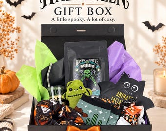 Puede incluir: Una caja de regalo negra con un lazo naranja que contiene una bolsa de café Bones, un monstruo de peluche verde, calcetines estampados, una pajita de metal, un vaso y una mascarilla facial con forma de murciélago. Dice HALLOWEEN GIFT BOX.