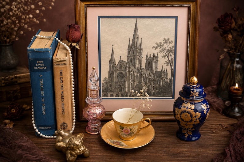 May include: A framed black and white architectural print of a cathedral, two vintage books, a pearl necklace, a pink glass perfume bottle, a gold-toned teacup and saucer with floral patterns, and a blue and gold lidded porcelain jar.