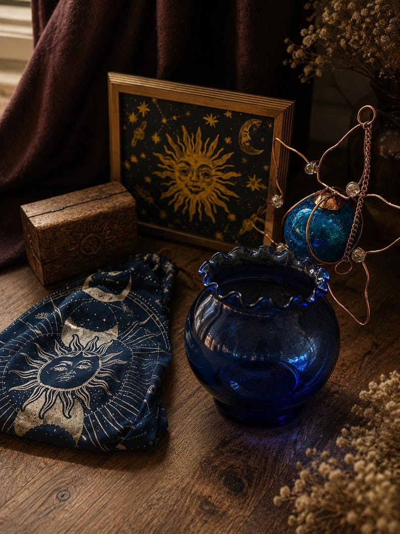 May include: A dark blue glass bowl with a ruffled rim, a navy fabric drawstring pouch featuring a gold sun and moon print, a small wooden box with a sun carving, a framed celestial print, and a copper wire star ornament with clear beads.