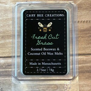 Peut inclure: Un contenant en plastique transparent contenant un fondant parfumé. L'étiquette noire indique "CARY BEE CREATIONS" et "Fresh Cut Grass". Il est également indiqué "Scented Beeswax & Coconut Oil Wax Melts" et "Made in Massachusetts". Le fondant pèse 78g.