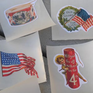 May include: A selection of vintage-style stickers with patriotic designs. The stickers depict an American flag, a drum, and a firecracker with the text "Will you go off with me on the 4th". They are presented on a light-coloured background.