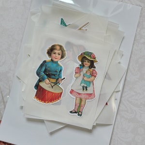 May include: A selection of vintage-style stickers featuring children. One sticker shows a boy in a blue uniform playing a red drum. Another depicts a girl holding a doll and a small American flag. The stickers are packaged in a clear plastic bag.